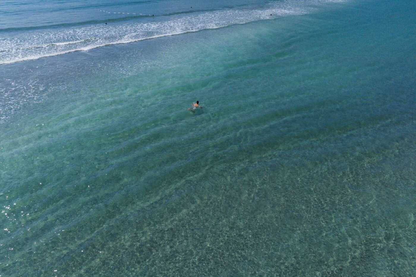 นักว่ายน้ำหนึ่งคนในน้ำตื้นใสของชายหาดโอกิตสึ