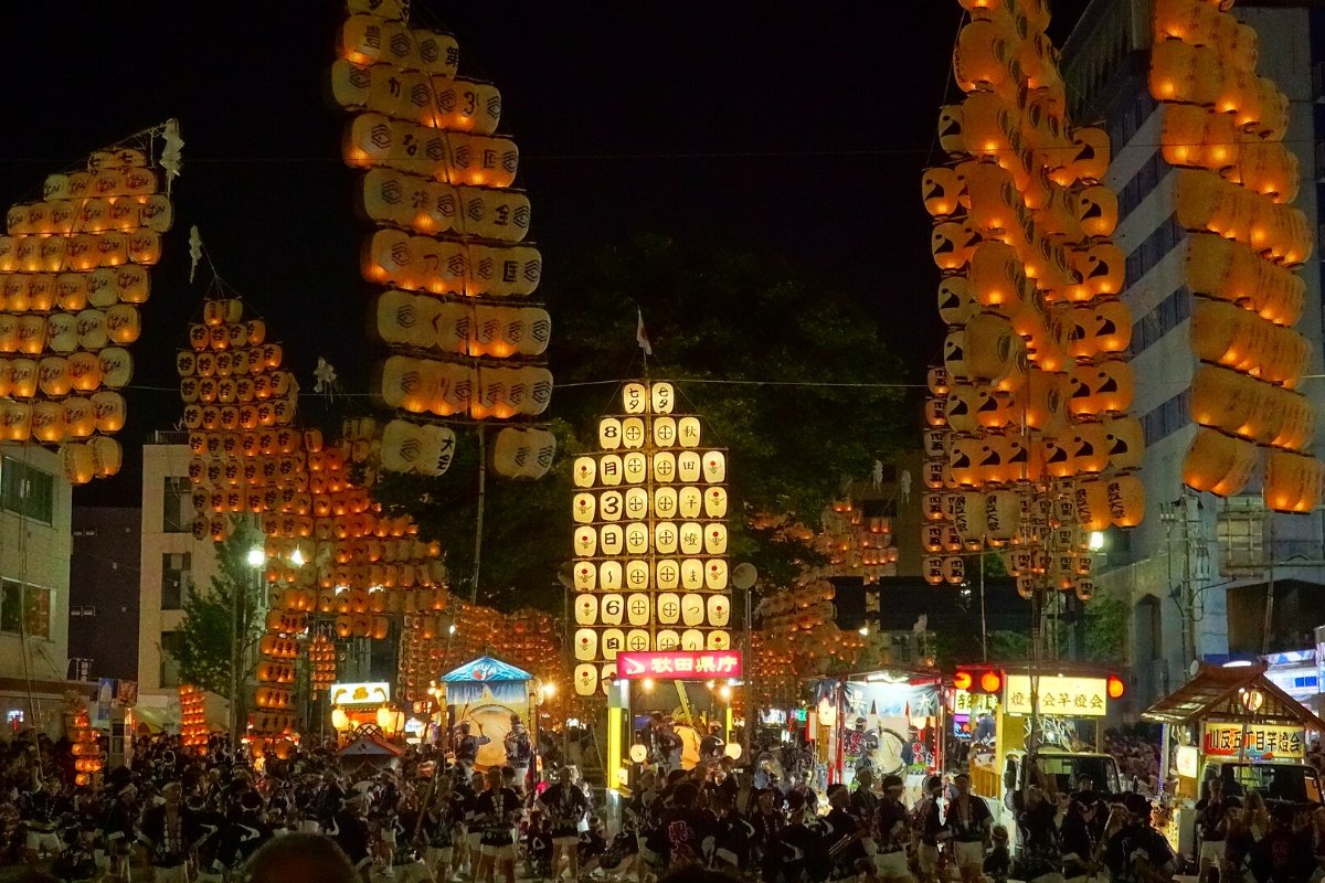 ผู้แสดงทรงคันโตะที่ติดโคมไฟเรียงเป็นแถวกลางถนนยามค่ำ ผู้ชมแน่นสองข้างทาง เมืองอาคิตะ จังหวัดอาคิตะ