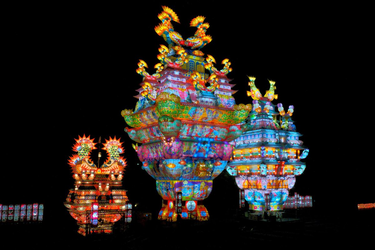 โคมปราสาทขนาดยักษ์สูงกว่า 20 เมตรส่องไฟกลางถนนยามค่ำ ผู้คนยืนชมสองข้างทาง เมืองโนชิโระ จังหวัดอาคิตะ