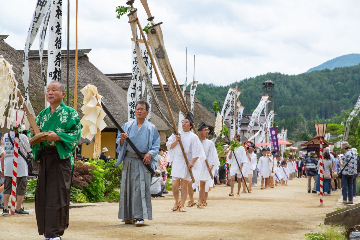 ขบวนมิโคชิและผู้ชายชุดขาวสวมหมวกเอโบชิเดินในหมู่บ้านโออุจิจุกุ เมืองชิโมโกะ จังหวัดฟุกุชิมะ