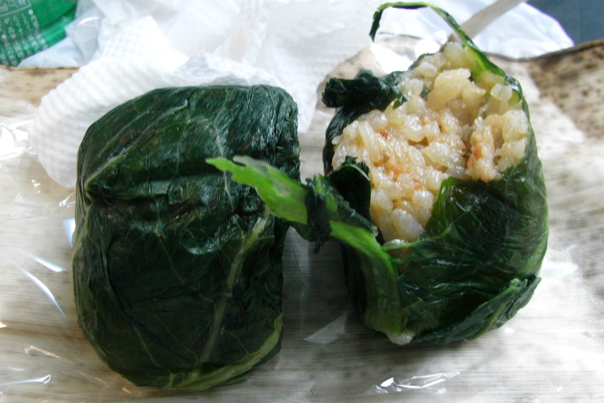 ข้าวปั้นก้อนกลมห่อด้วยใบผักดองสีเขียวเข้มวางบนจาน อาหารพื้นบ้านทางใต้ของนารา