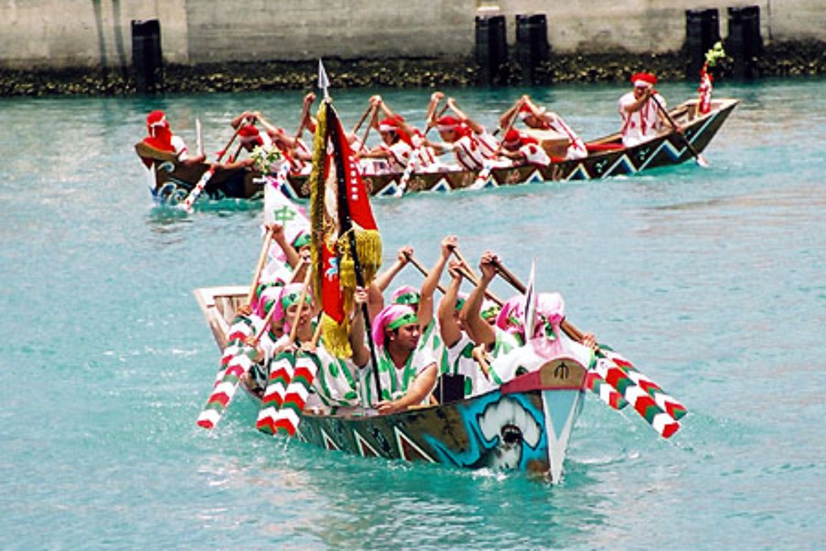 เรือมังกรหลายลำพายแข่งกันในท่าเรือประมงอิโตมัน มีผู้ชมยืนเต็มริมท่า
