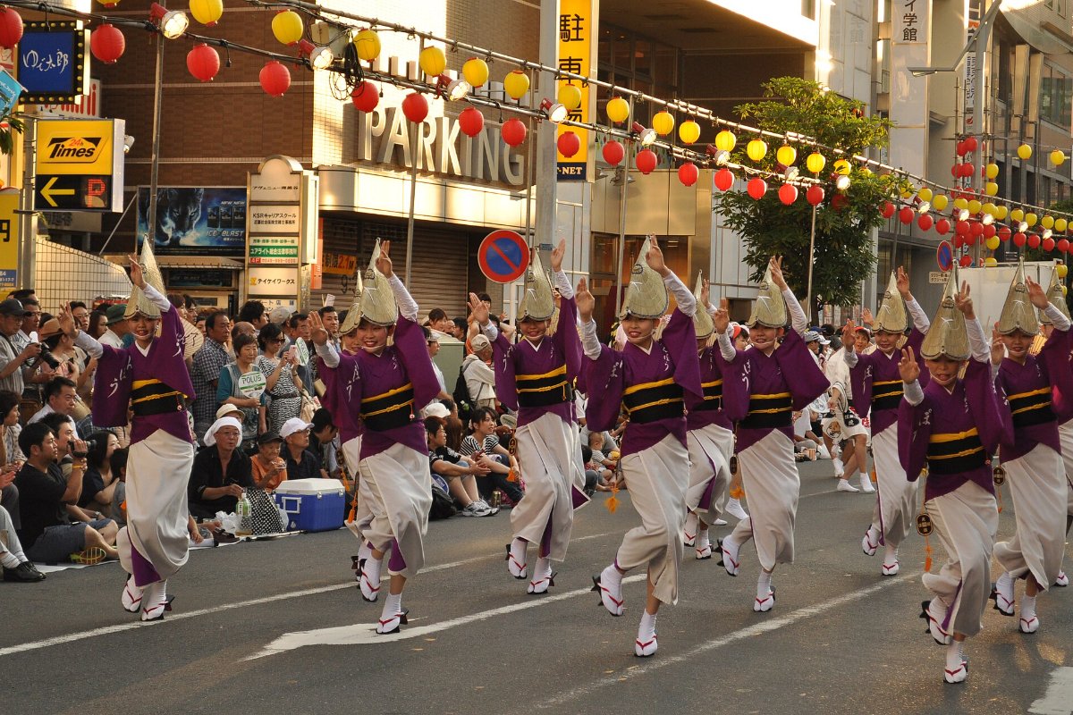 คณะระบำอาวะโอโดริในชุดยูกาตะและหมวกฟางเต้นเป็นแถวบนถนนยามค่ำ มินามิโคชิงายะ